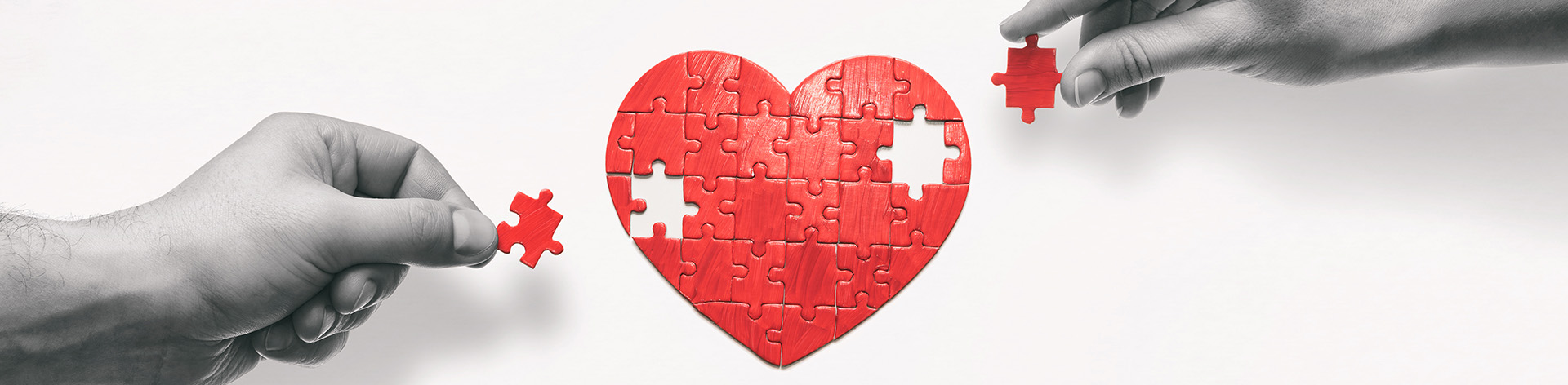 Hands reach toward a puzzle shaped like a heart.